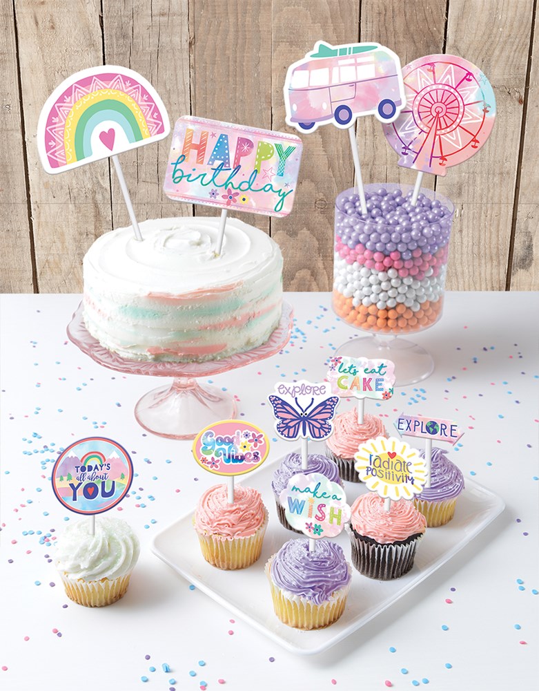 Colorful paper toppers including rainbow, camper, ferris wheel, and "Happy Birthday" text on white cake and pastel-frosted.