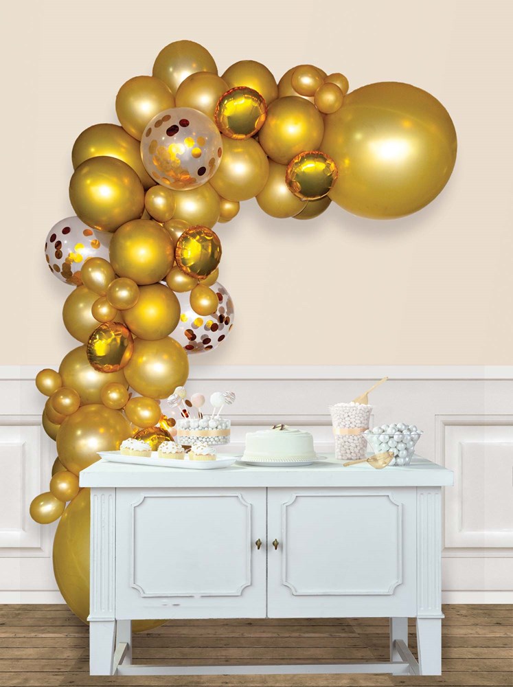 Gold metallic balloon garland arch with various sizes and confetti-filled balloons over white sideboard.