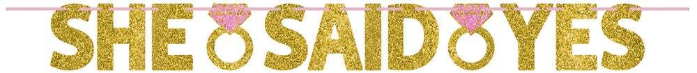 Gold glitter "SHE SAID YES" letter banner with pink engagement ring icons between words.