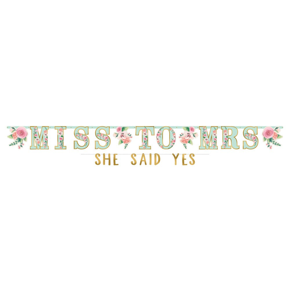 Floral patterned jumbo letter banner in pastel green and pink spelling "MISS TO MRS" with gold foil "SHE SAID YES" text.