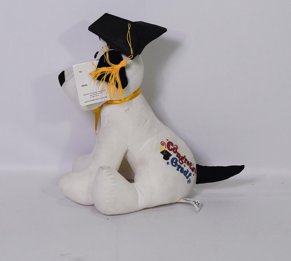 White plush dog with black ears and tail wearing a black graduation cap holding a pen in its mouth and a yellow ribbon.