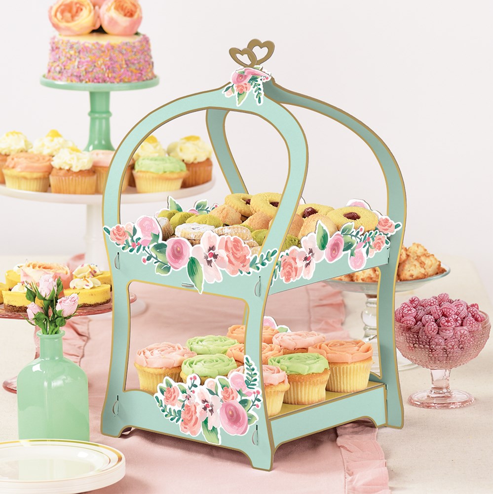 Mint green wooden treat stand with floral accents and heart-shaped top handle, holding cupcakes and treats.