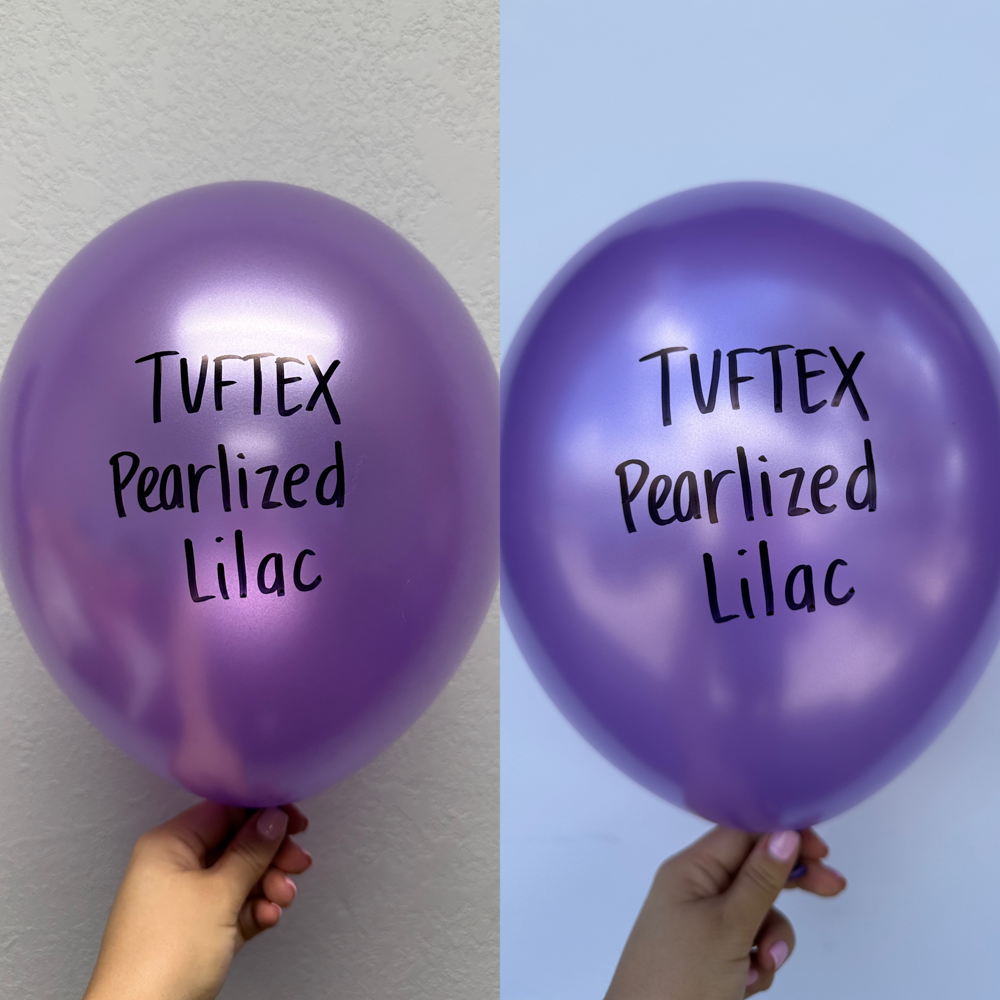 Two metallic pearlescent lilac latex balloons, round and shiny, held against a plain light wall background.