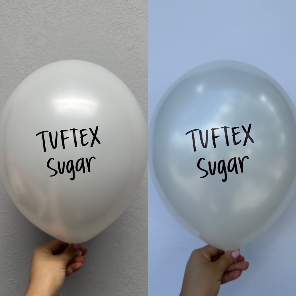 Set of two white 5-inch latex balloons with "TUF TEX Sugar" printed in black on front, held by hand against gray and blue.