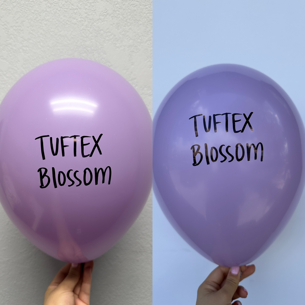 Two glossy latex balloons in shades of purple with "Tuftex Blossom" text printed in black, each held by a hand against plain