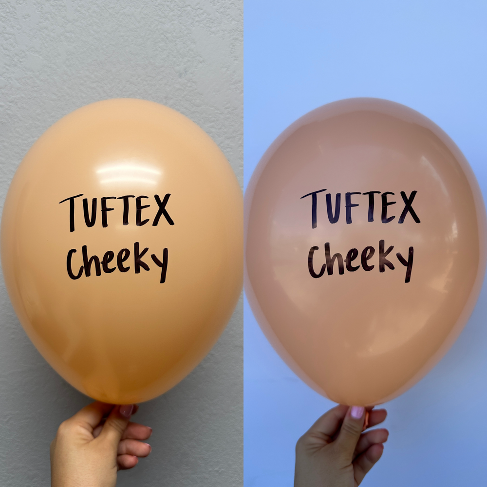 Two 17-inch latex balloons in peachy-orange color, each printed with "Tuftex Cheeky" in black font, held by hand against.