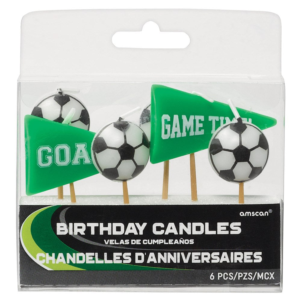 Six colorful birthday candles shaped like soccer balls and green pennant flags with "GOAL" and "GAME TIME" text, on wooden.