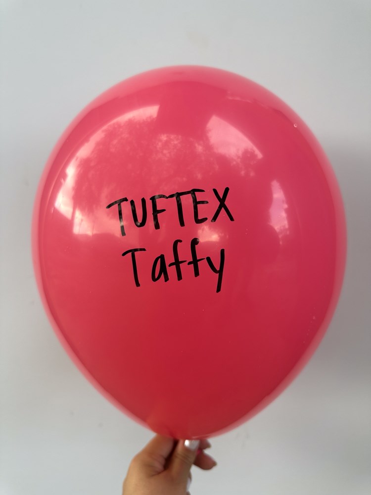 Glossy pink latex balloon with black "TUFTEK Taffy" text, 17 inches, inflated and held by hand.