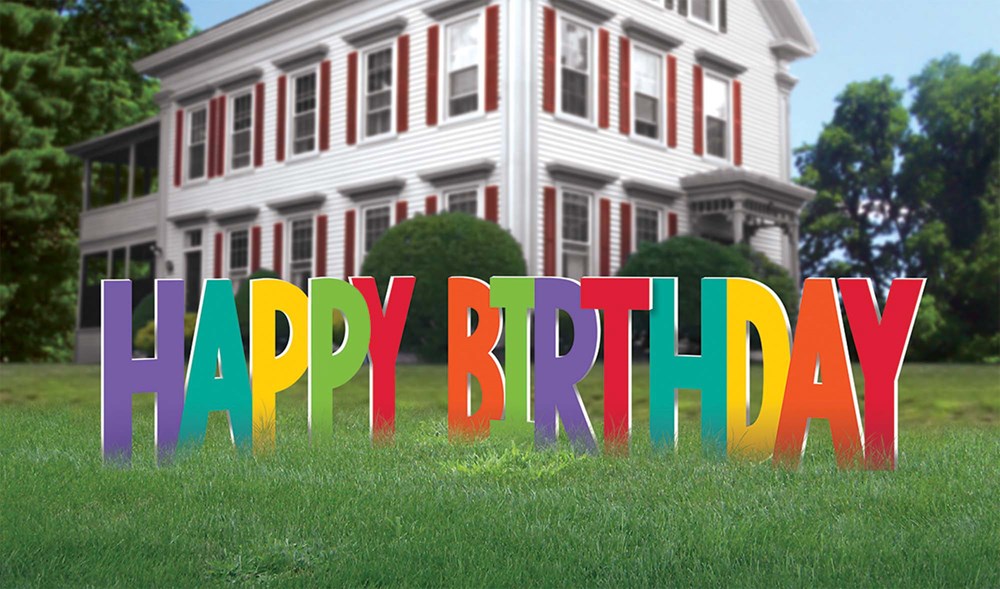 Colorful large block letters spelling "Happy Birthday" in rainbow colors, designed as a yard sign on a lawn.