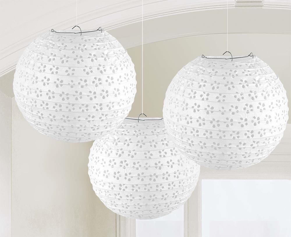 Three white round paper lanterns with floral eyelet cutout patterns hanging indoors.