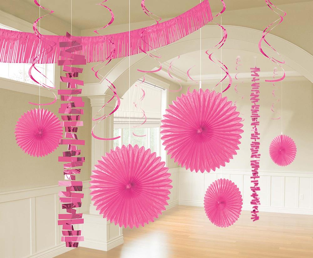 Bright pink hanging paper fans and curly streamers decorating a room ceiling for a party.