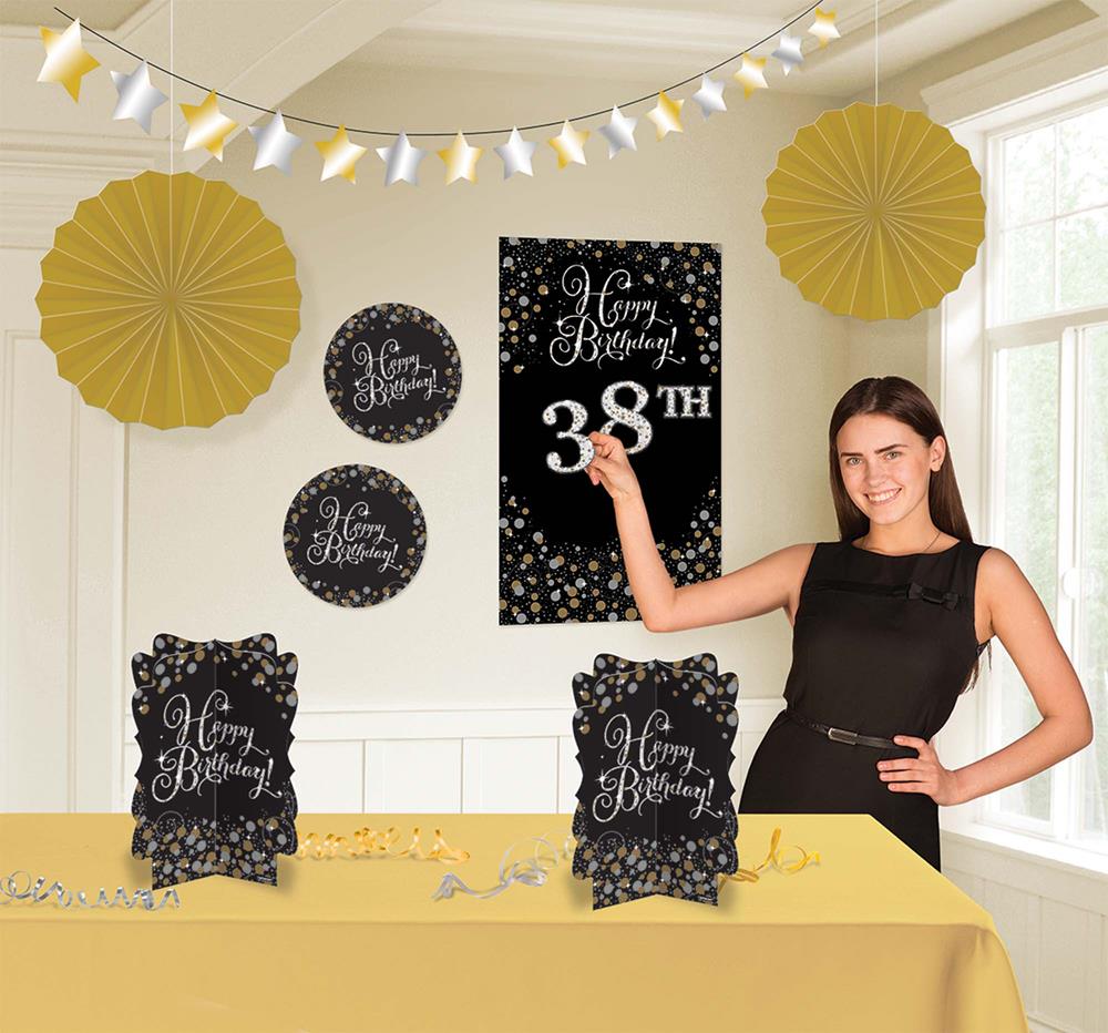 Gold paper fans and white star garlands with black and gold "Happy Birthday" signs decorating a room with a woman in a black .