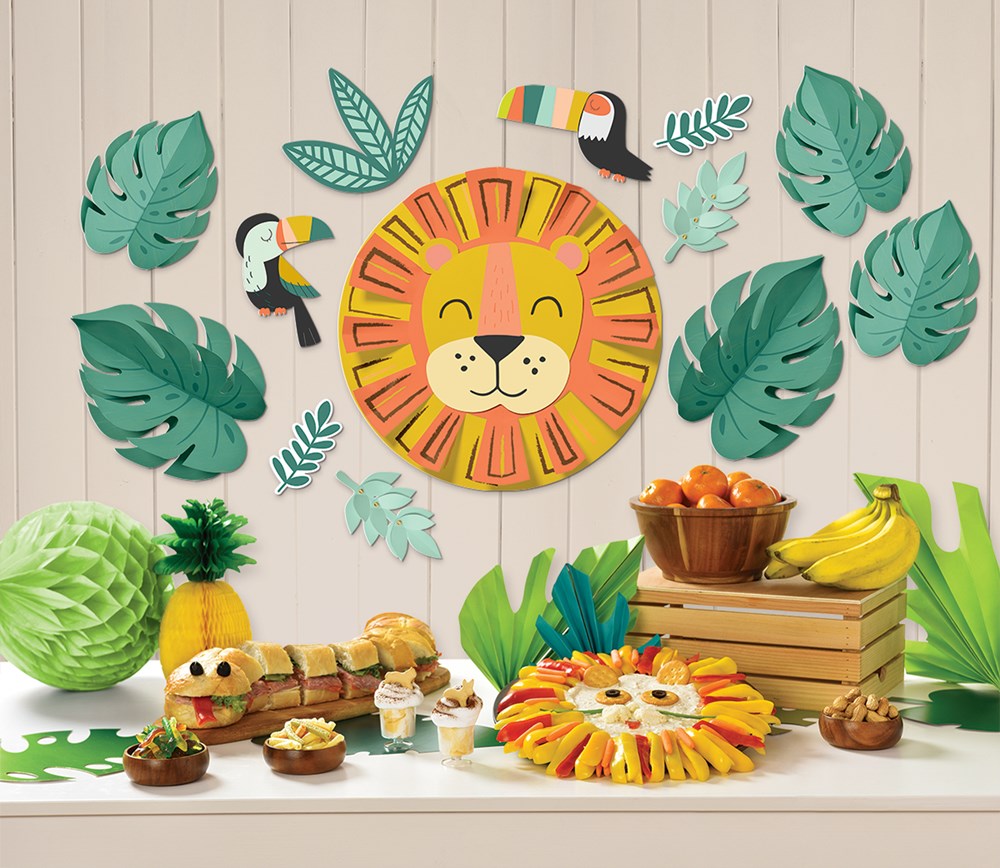 Colorful lion face centerpiece with toucan and green tropical leaf wall decorations in animal party theme.
