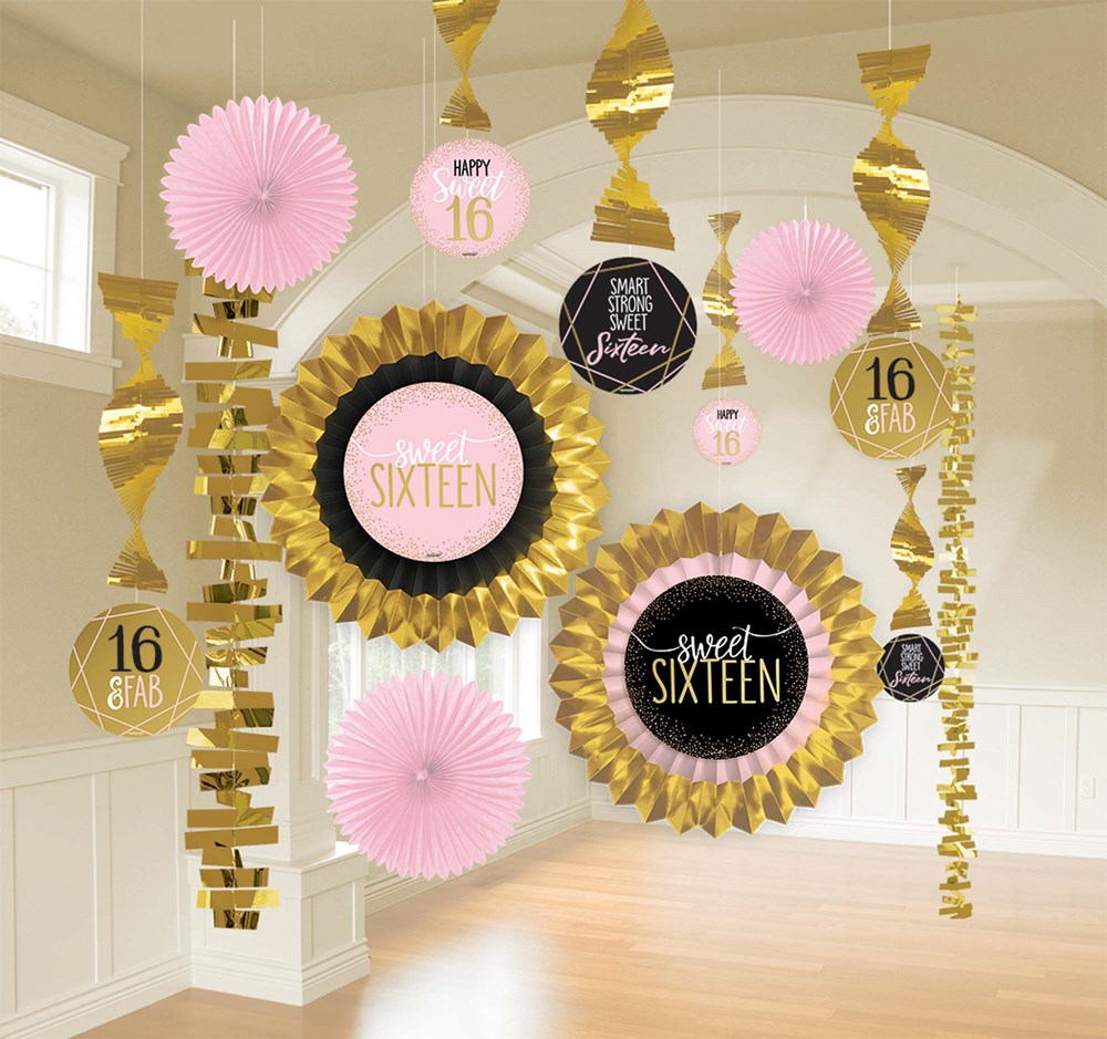 Blush pink, gold, white, and black paper rosettes and hanging spirals with "Sweet Sixteen" and "16" text decorations.