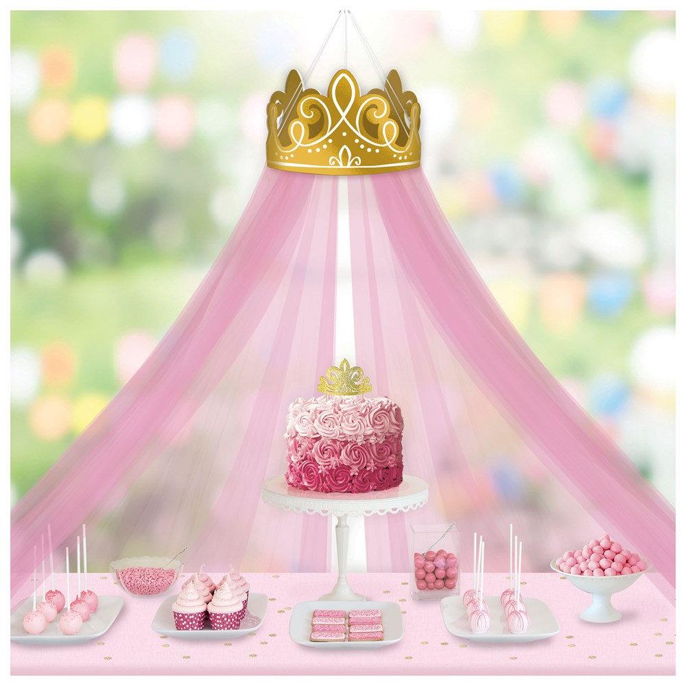 Gold crown wall decoration with flowing pink tulle canopy over pink ombré birthday cake and matching pink dessert table.