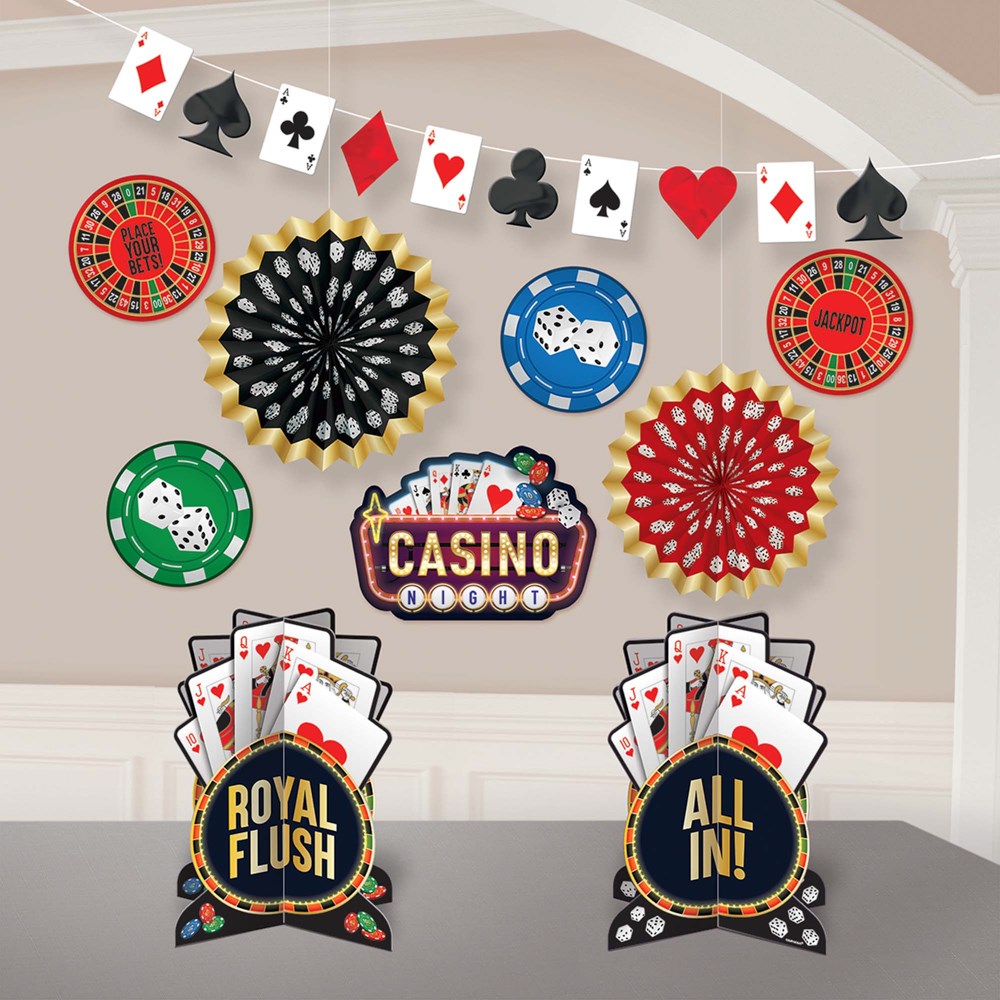Casino-themed hanging decorations with playing card suits, poker chips, black and red fan rosettes, and signs reading "Royal