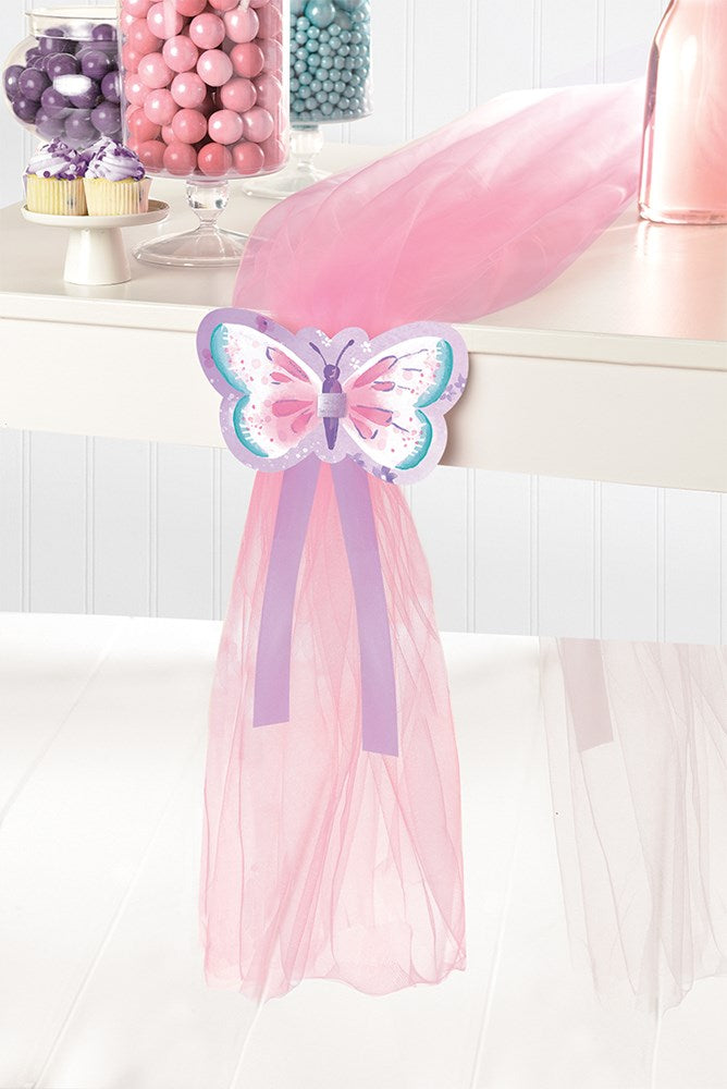 Pink sheer table runner decorated with a multicolored butterfly cutout and trailing purple ribbons.