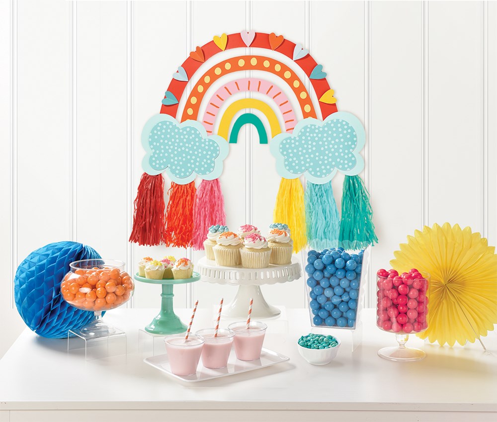 Retro rainbow wall hanging with tasseled arches in red, orange, yellow, green, and blue, decorated with two blue clouds and.