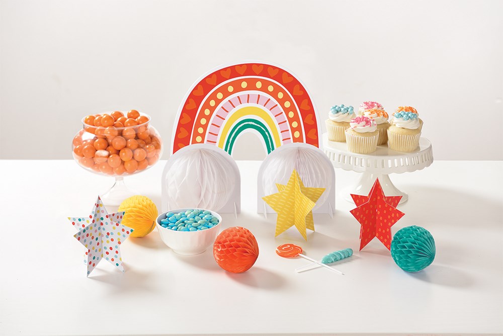 Colorful retro rainbow paper fan, star-shaped tissue decorations, orange pom-poms, blue confetti, and birthday party.
