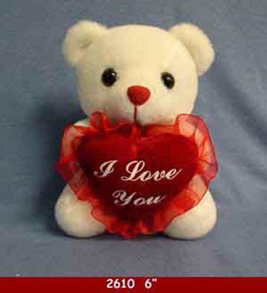 Small white plush teddy bear holding a red heart-shaped pillow with "I Love You" in white script and ruffled edges.