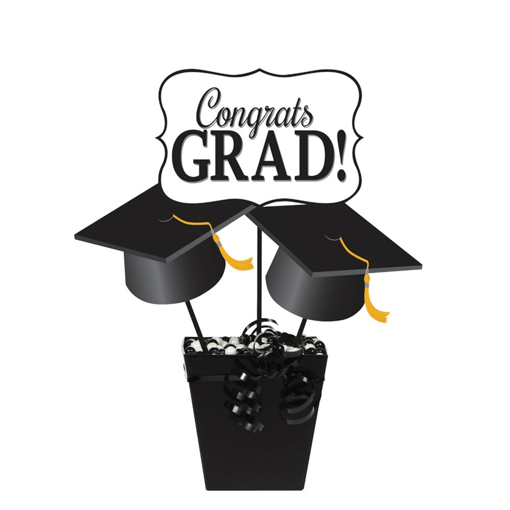 Black paper container holding three centerpiece sticks with black graduation caps and a white sign reading "Congrats GRAD!".