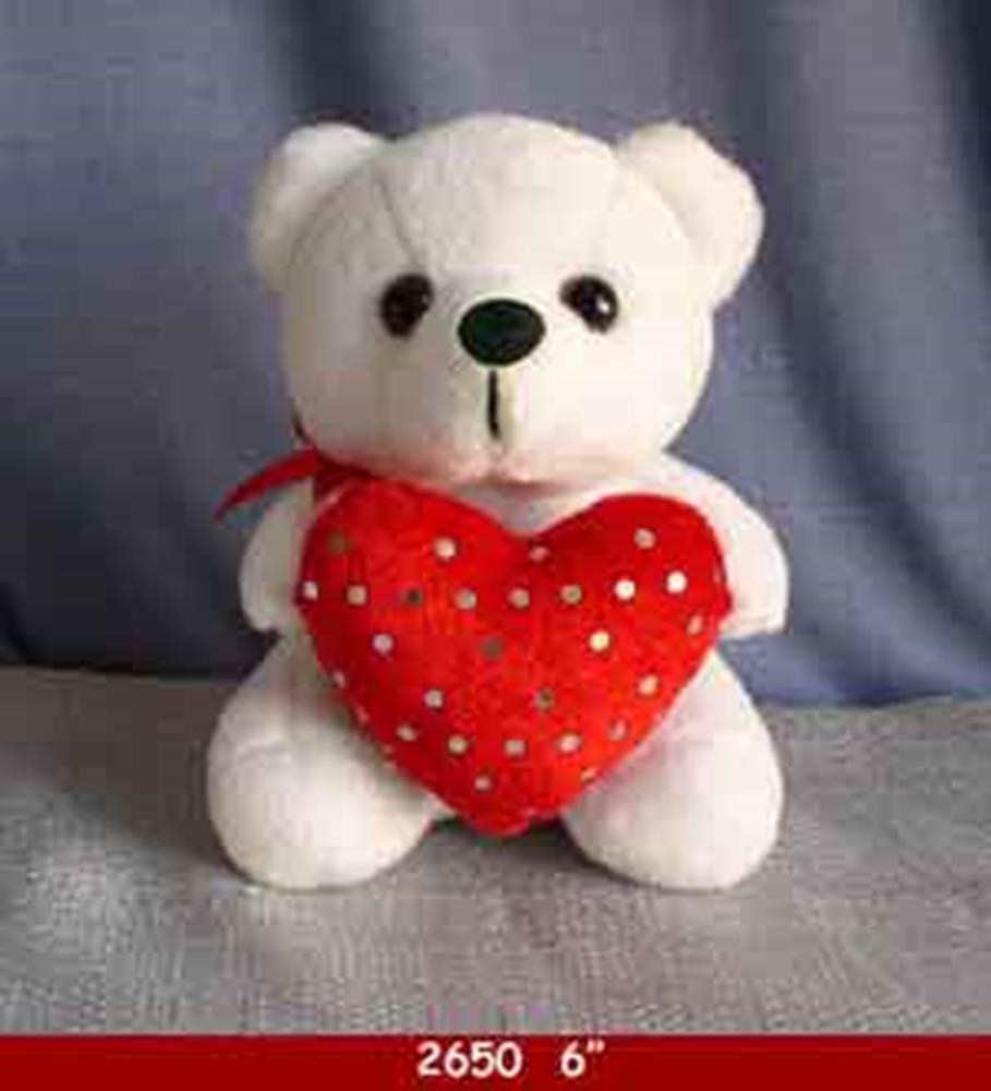 White plush teddy bear holding a red heart with small silver polka dots and a red ribbon around its neck.