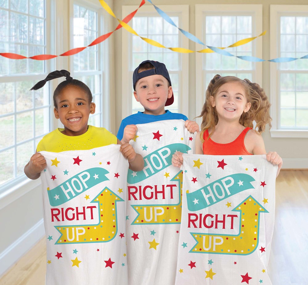 Three kids holding colorful fabric potato sacks with "Hop Right Up" text and star designs for party games.