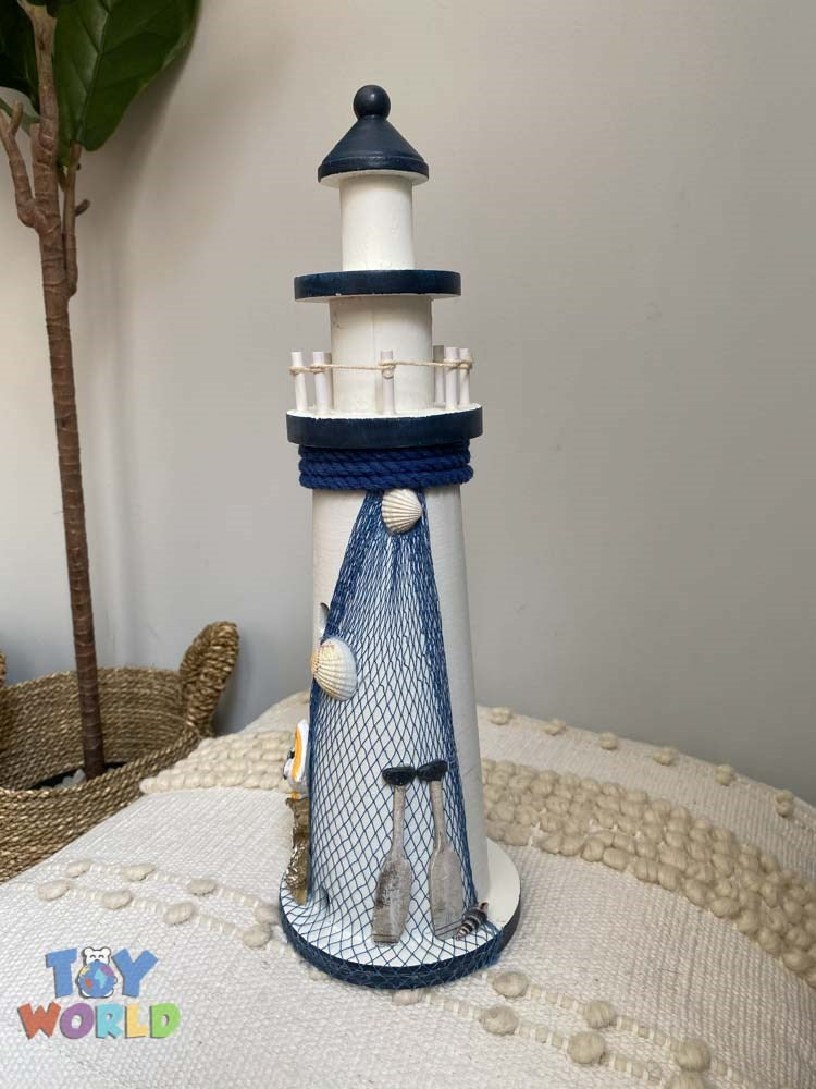 Tall wooden lighthouse decoration painted white and navy blue with rope, fishing net, seashells, and anchor accents.