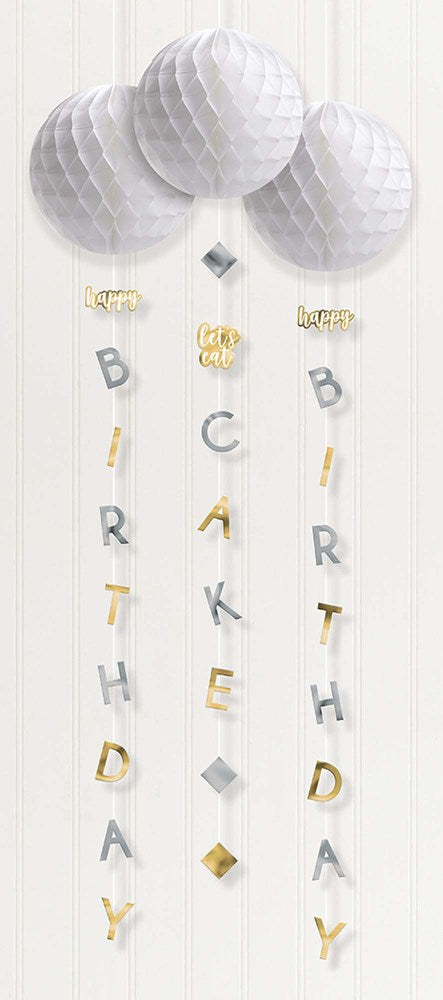 Three silver and gold honeycomb paper balls with hanging gold letter garlands spelling "BIRTHDAY" and "CAKE".