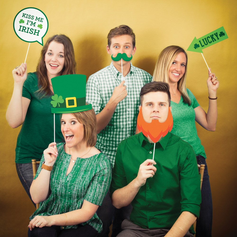 Group of four adults holding St Patrick’s Day photo props including a green leprechaun hat, a green shamrock mustache, a red