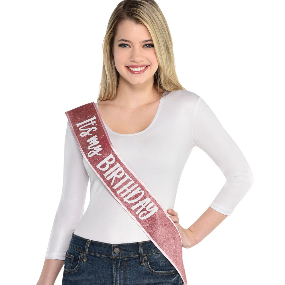 Blush pink satin sash with white script reading "It’s My Birthday" worn diagonally across the torso.