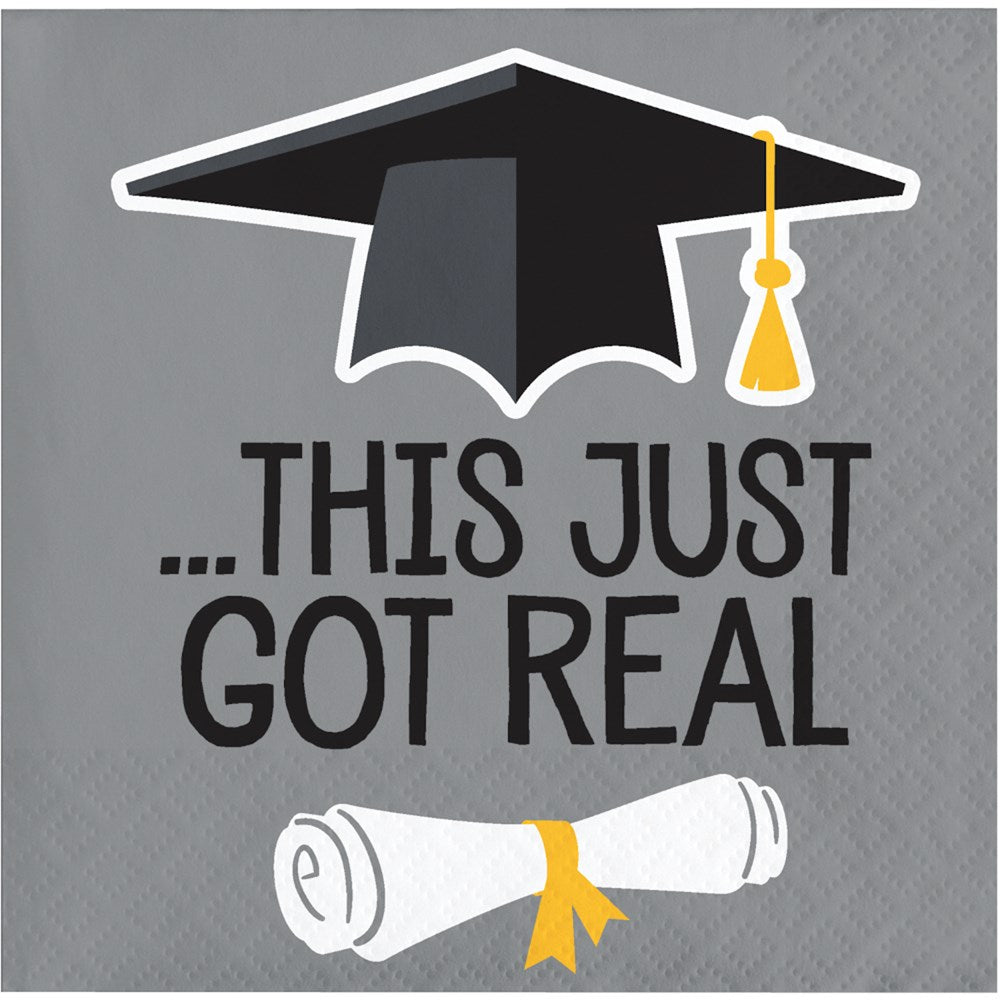 Gray beverage napkin with black graduation cap and yellow tassel above text "This Just Got Real" and rolled diploma tied.