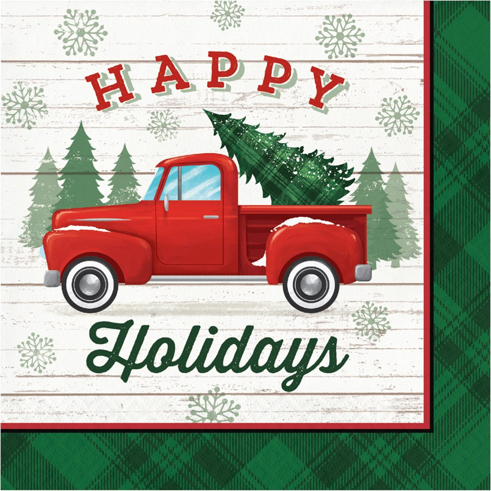 Stack of square Christmas napkins with red vintage truck carrying a green Christmas tree, "Happy Holidays" text, white wood.