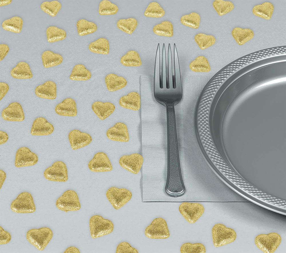 Small shiny gold heart-shaped table scatters spread across a white surface next to a silver fork and textured silver plate.