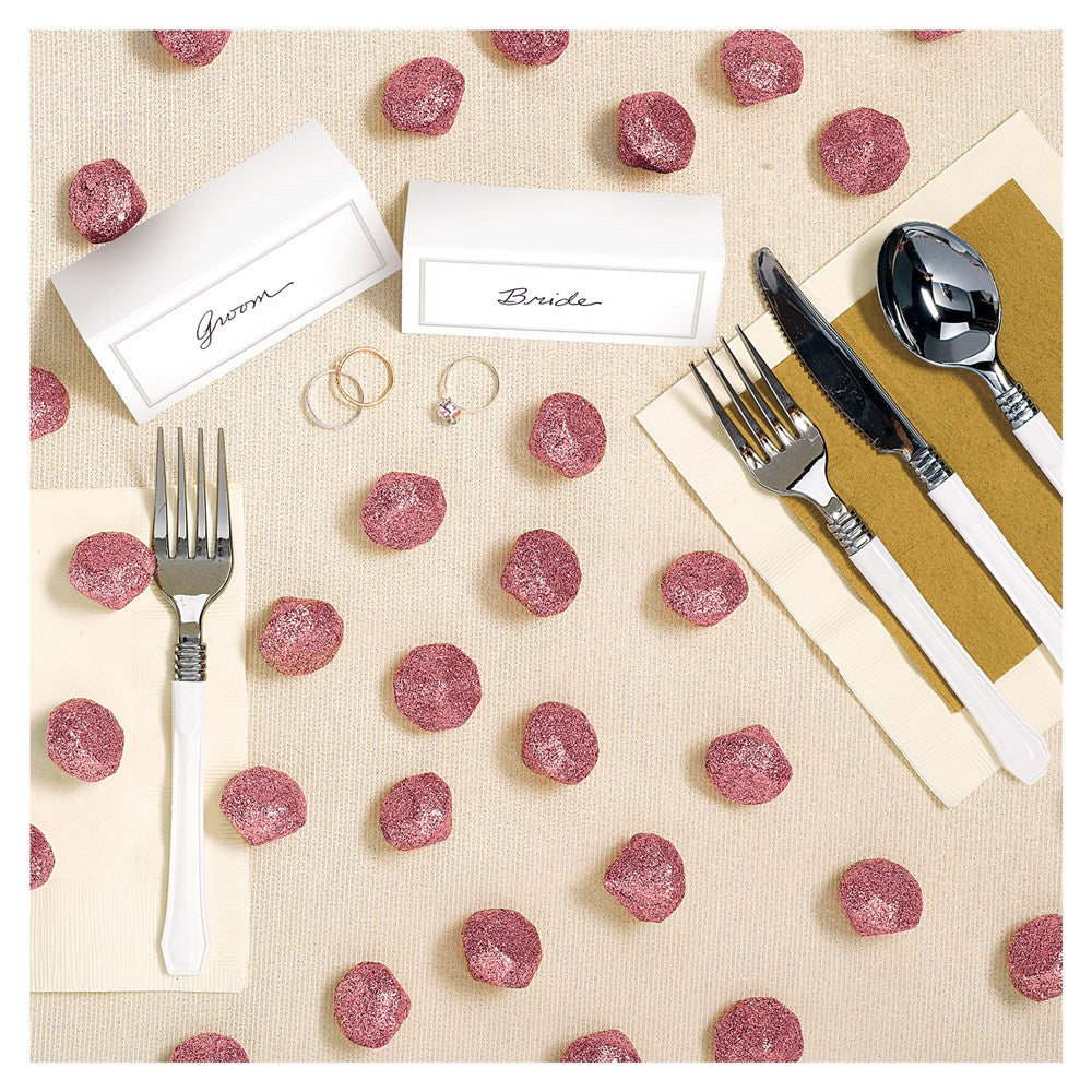 Pink glittery diamond-shaped table scatters scattered on a beige tablecloth around cutlery and place cards.