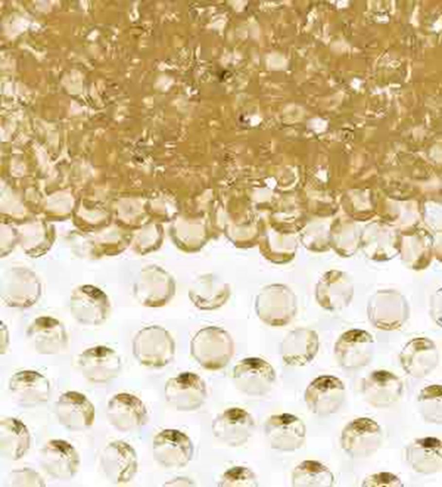 Scattered small round gold plastic confetti gems with faceted surfaces reflecting light.