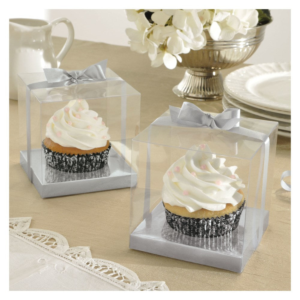 Clear plastic square cupcake boxes with silver bases and silver ribbon bows, holding frosted cupcakes.