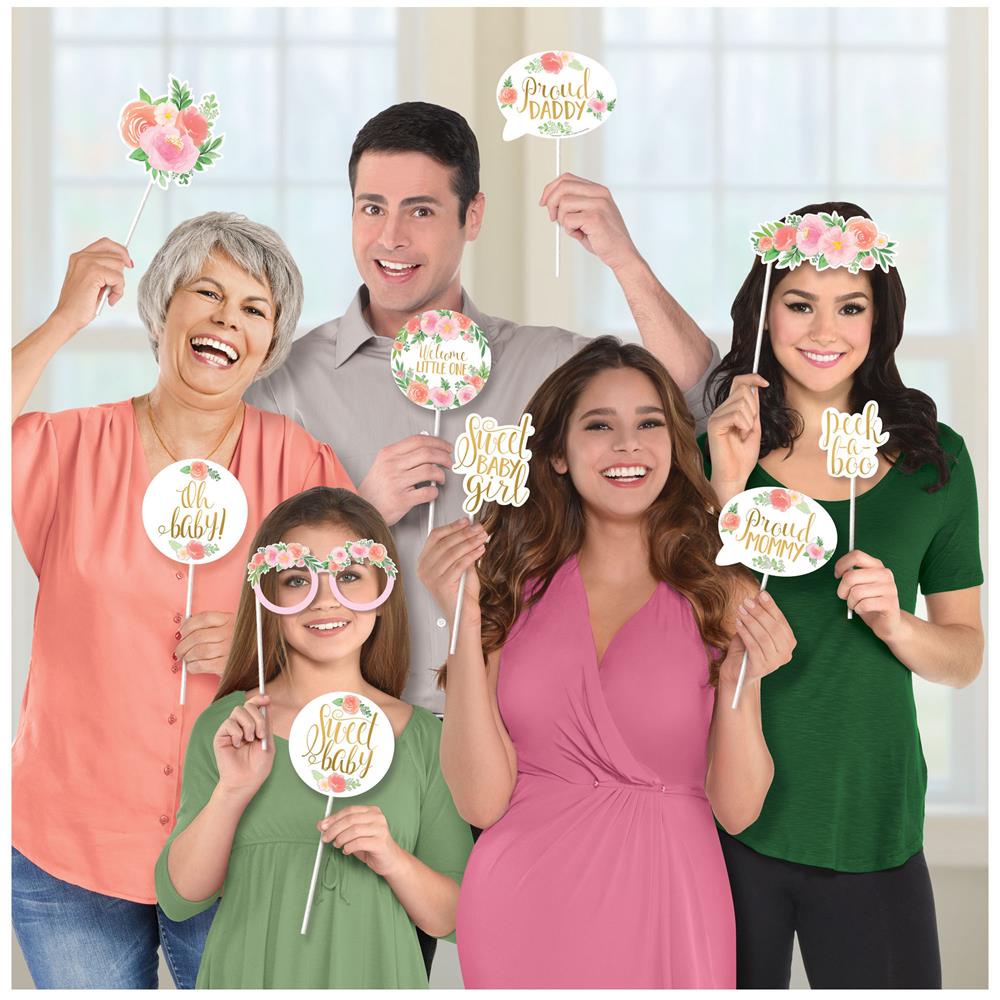 Floral baby photo props including flower crown, signs with gold text, and round floral patterns held by diverse group in.
