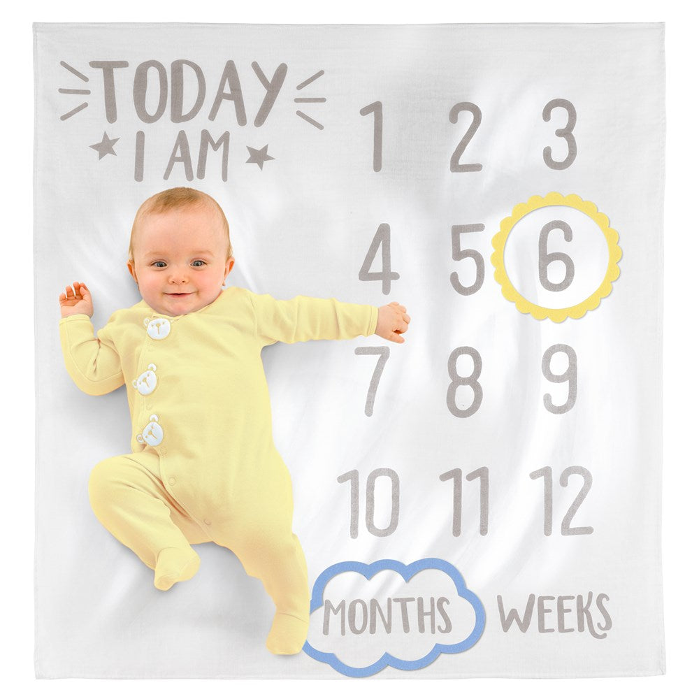 White baby milestone blanket with gray numbers 1 to 12, yellow circled 6, "Today I am" text, and a baby in yellow pajamas.