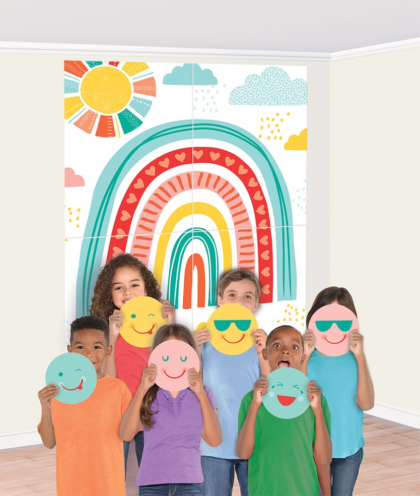 Colorful rainbow wall decal with sun and clouds, children holding jumbo smiley face props in various expressions.