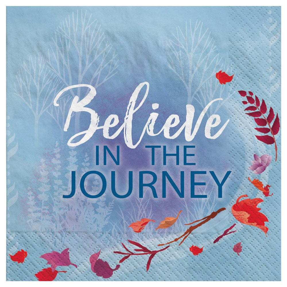 Blue square beverage napkin with "Believe in the Journey" text, red leaves, and subtle tree silhouettes.