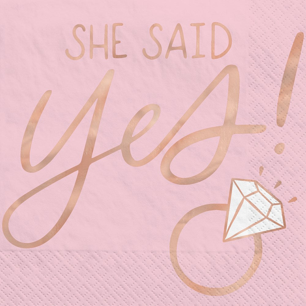 Light pink beverage napkin with rose gold foil text "She Said Yes!" and a diamond engagement ring graphic.
