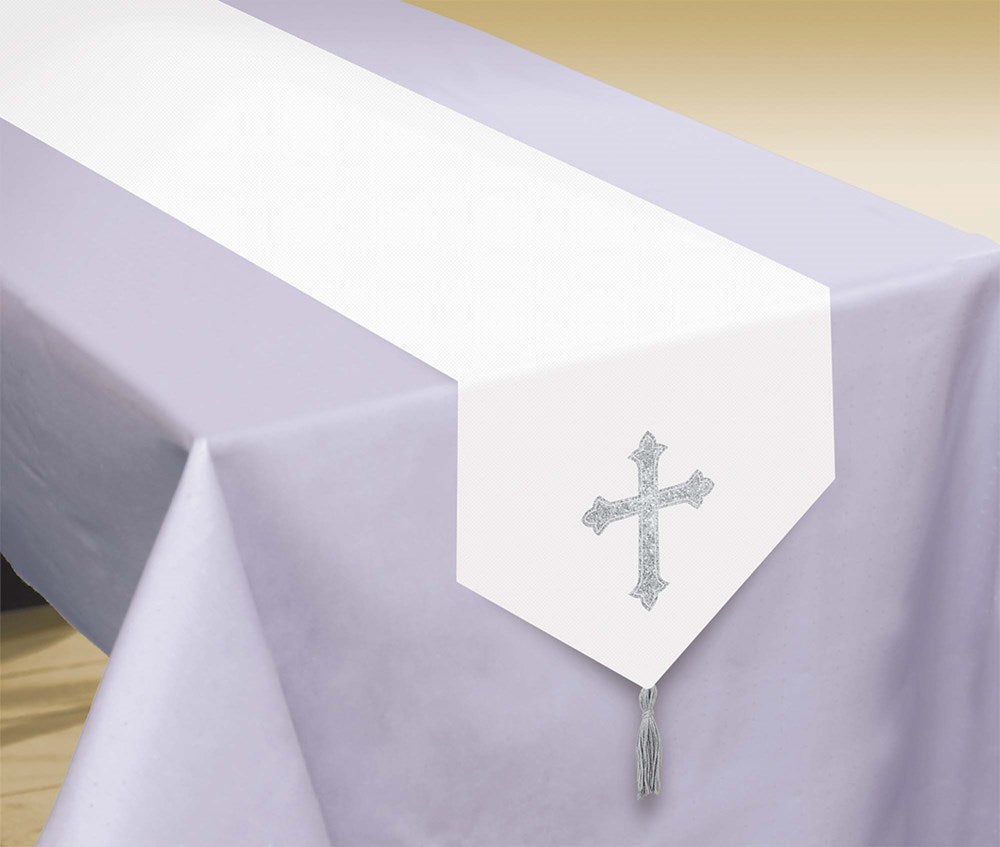 White table runner with silver glitter cross and tassel on light purple tablecloth.