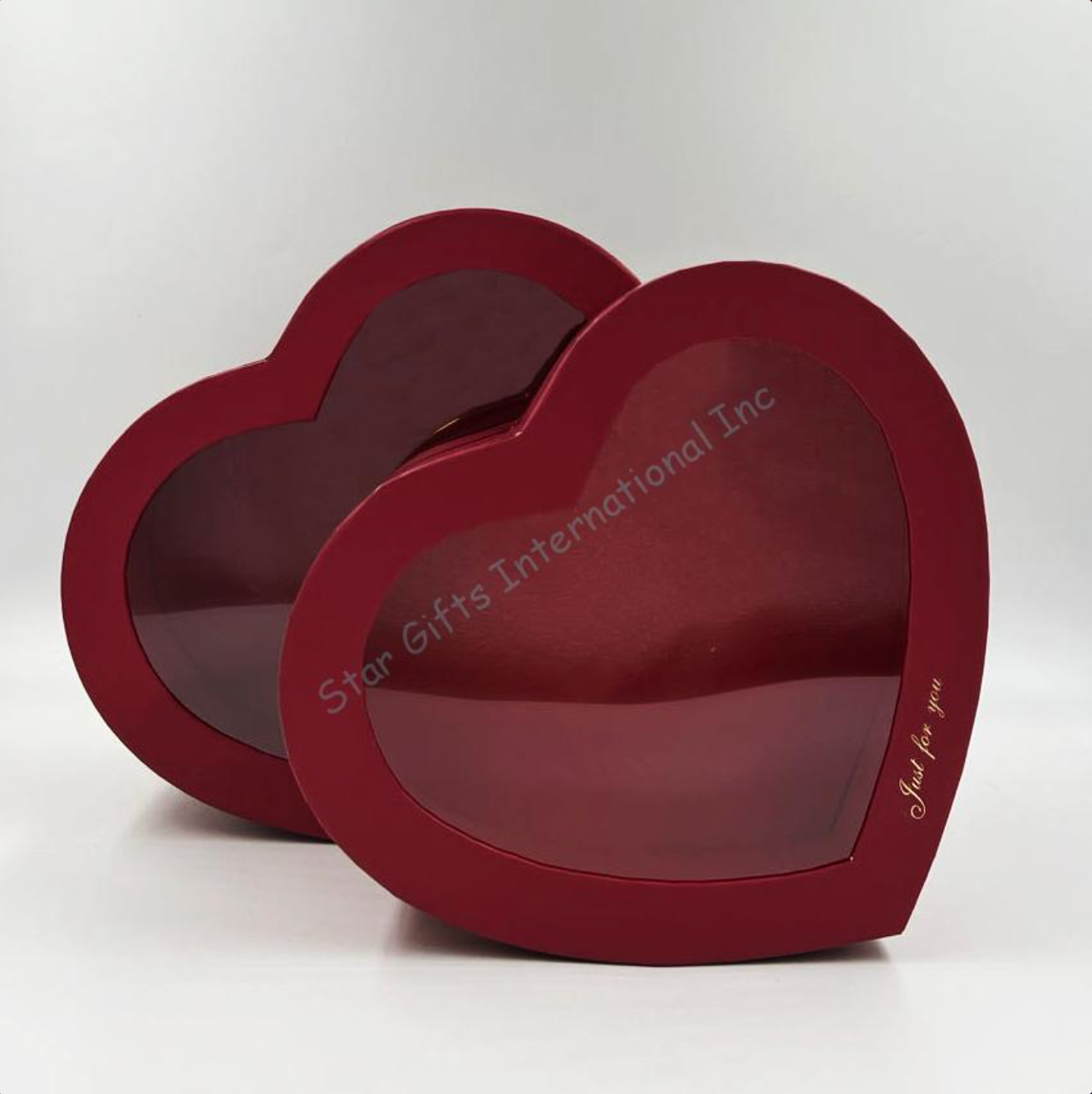 Two red heart-shaped gift boxes with clear plastic lids, one slightly smaller inside the larger one.