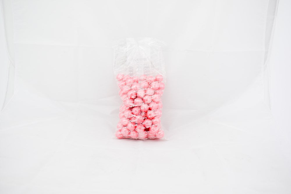 Clear plastic bag filled with bright pink, round gumballs against a white background.