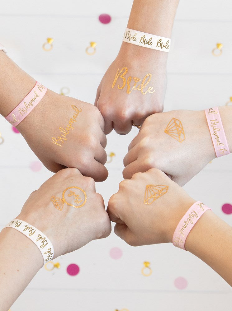 Set of five gold metallic temporary tattoos with bridal-themed designs on fists, paired with pale pink bachelorette.
