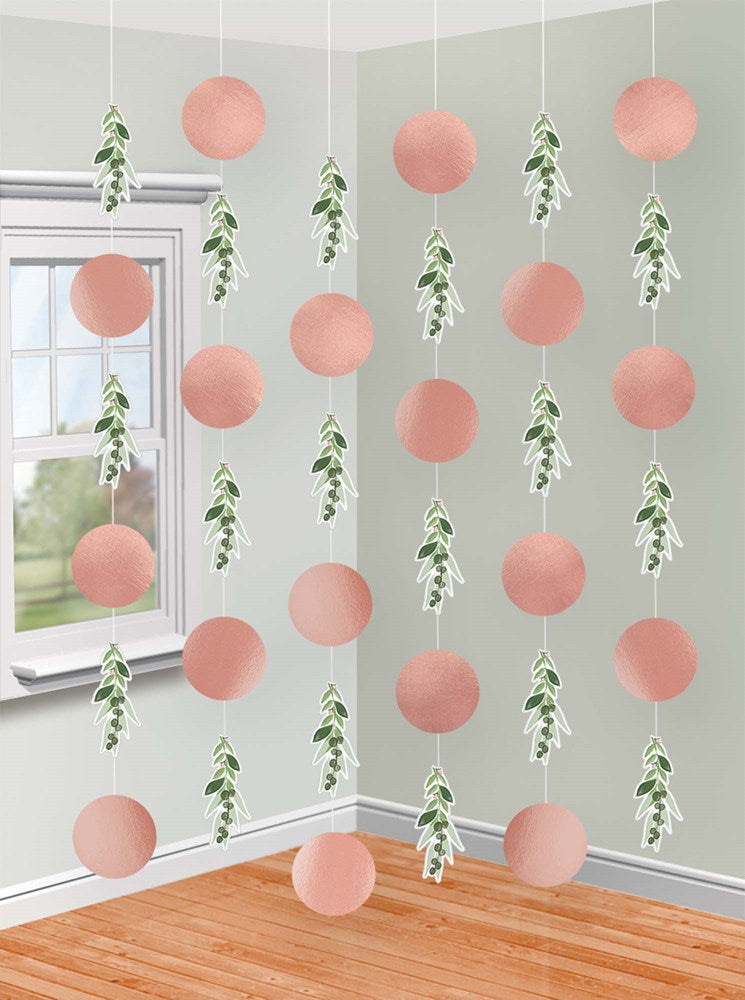 Strings of pink paper pom-poms alternating with green leafy garlands hanging vertically in a corner room.
