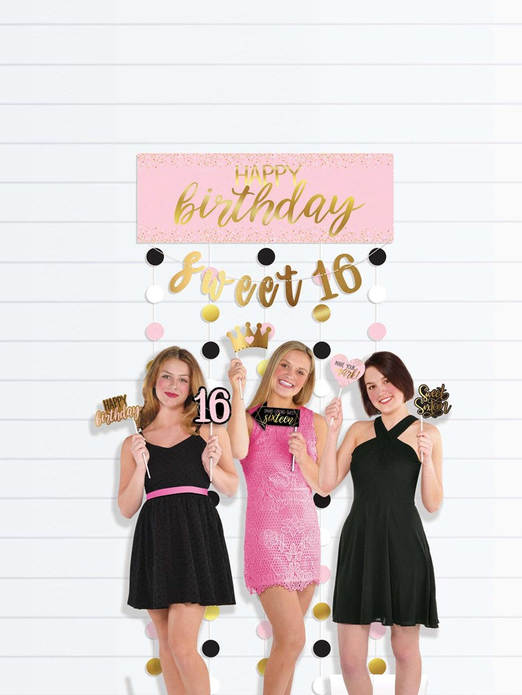 Blush and gold "Happy Birthday Sweet 16" banner with black, white, and gold pom-pom garland above three girls posing in.