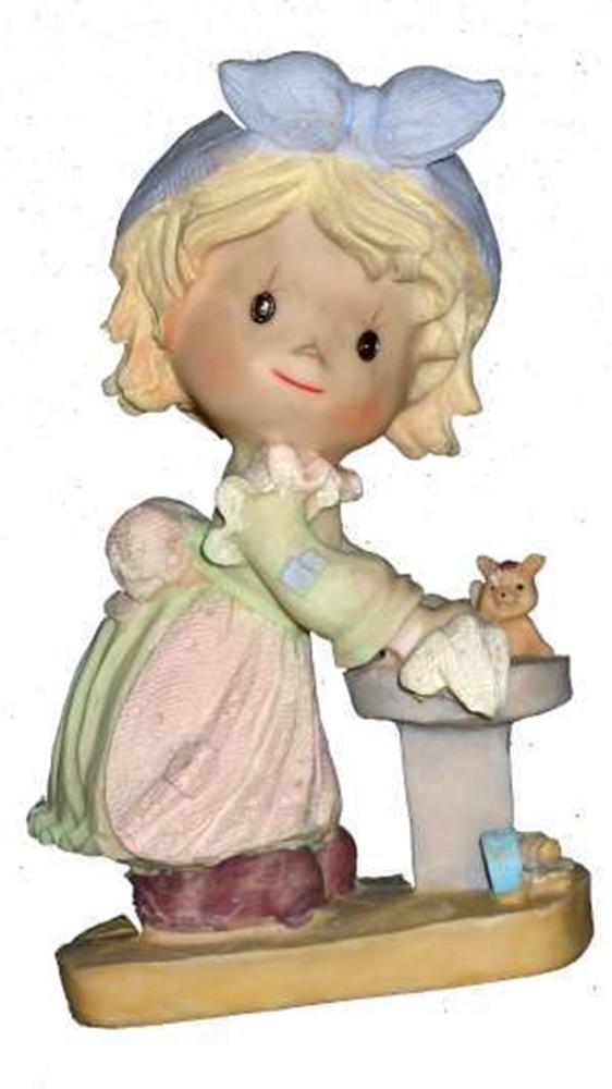 Small polystone figurine of a girl with blonde hair and blue bow, wearing pastel dress, holding a cleaning cloth by a small.