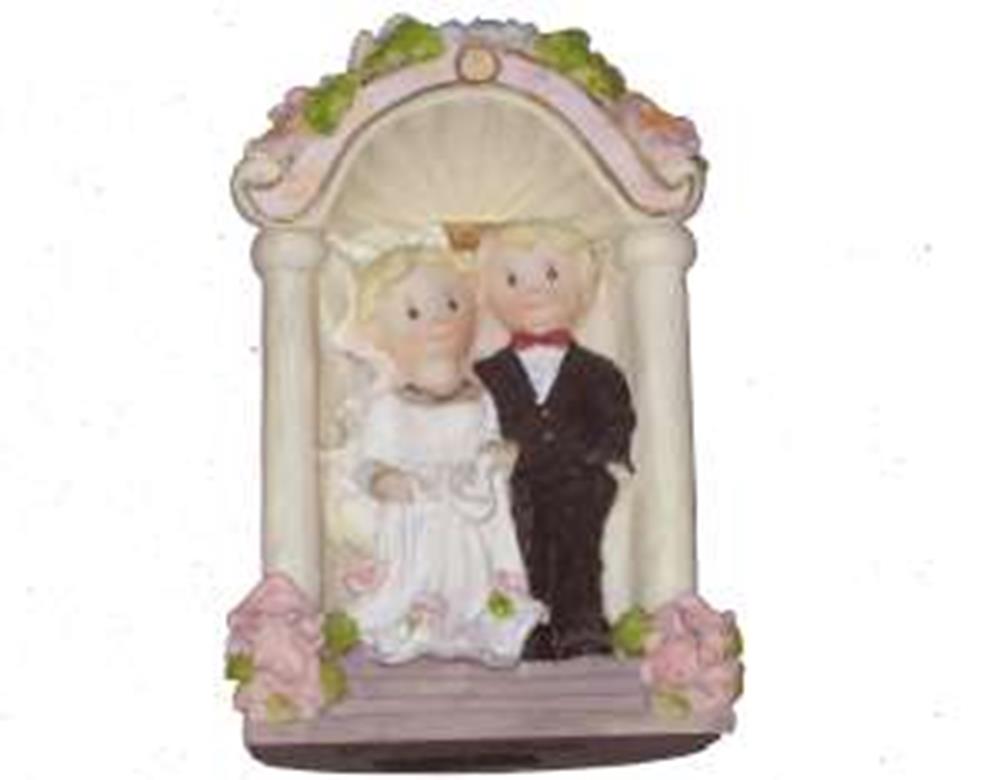 Polystone figurine of bride in white dress and groom in black tuxedo under floral arch with pink roses.